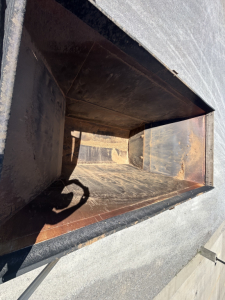 Trailer dumping bed interior showing rusty metal walls and empty chute near open top.