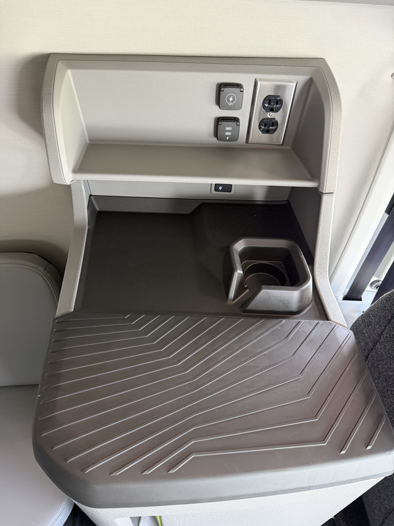 Cab interior featuring a small overhead shelf with two electrical outlets and a cup holder, view of a fold-down entry table in a Volvo VNL truck sleeper area.