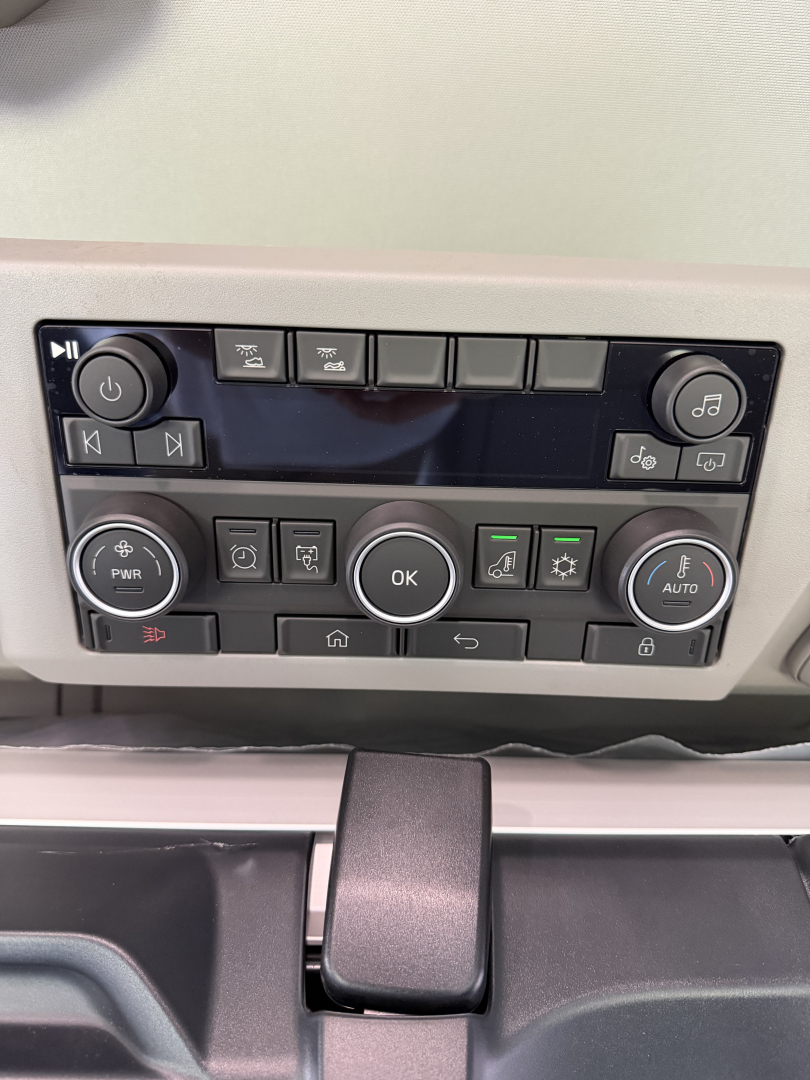 Dashboard control panel of a new Volvo VNL64T860 showing multiple circular and rectangular buttons and an OK center button.