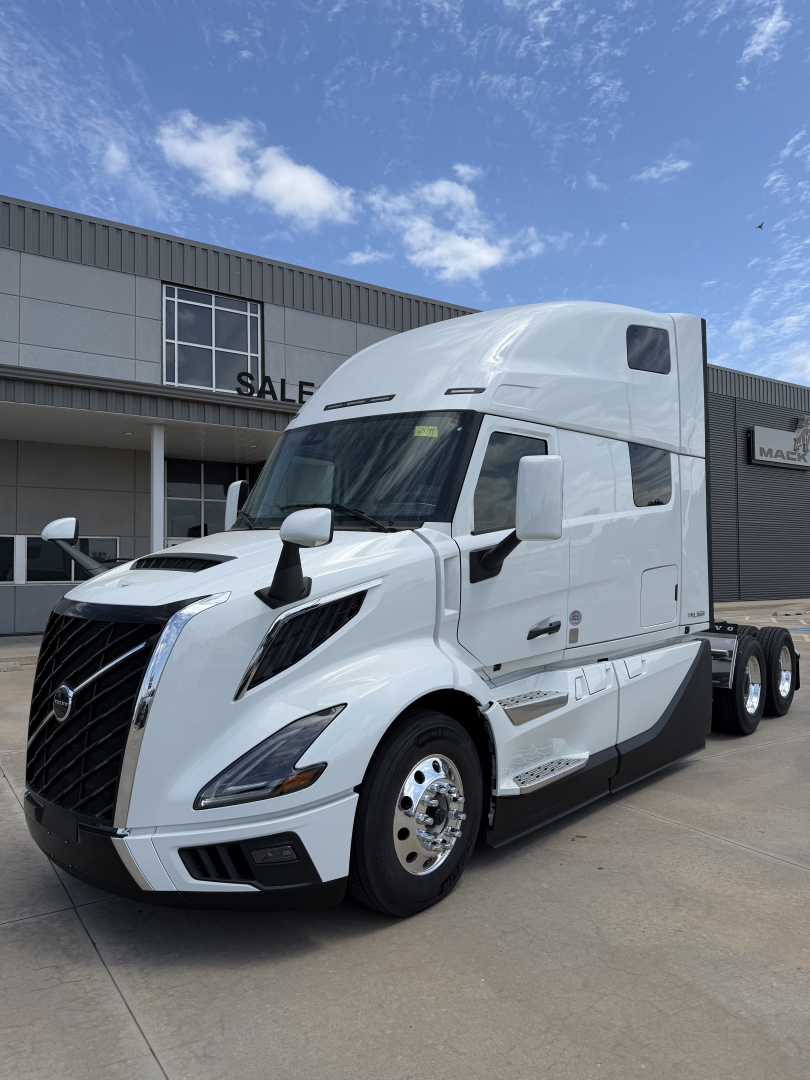 Truck front-left view of a new white Volvo VNL64T860 sleeper cab showing aerodynamic mirrors and large grille, center logo, twin rear axles visible.