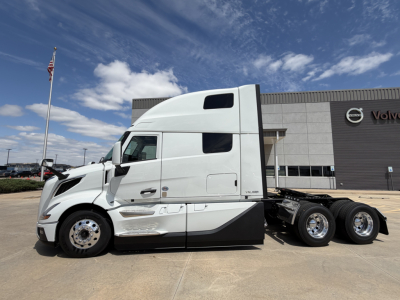 Volvo VNL64T860 truck tractor in white, side view, showing sleeper cab and rear dual axle, stationed in front of Volvo dealership.