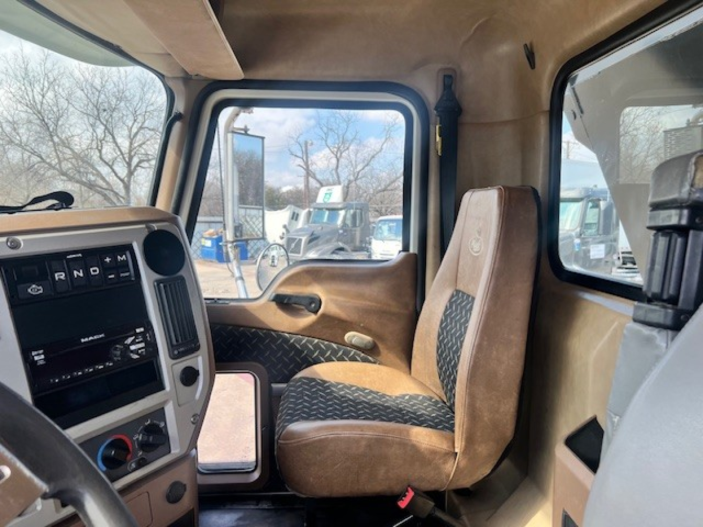 Cab interior of a 2018 Mack GU713 dump truck showing front seats, dashboard with gear selector, and side window view.