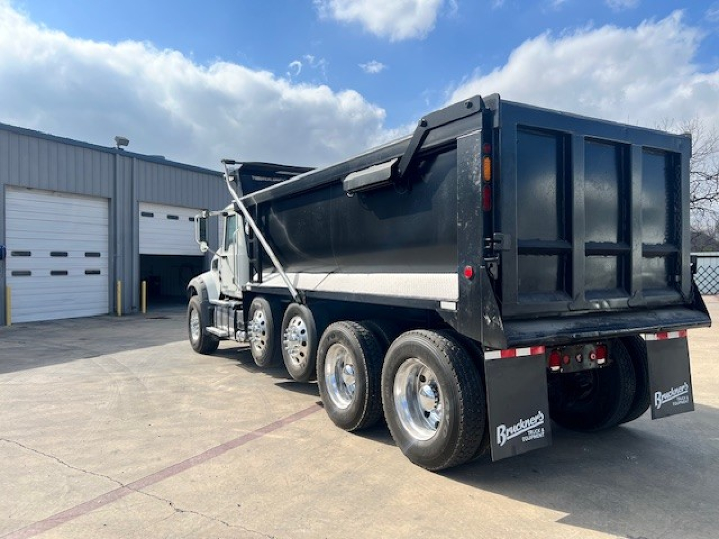 Dump truck in service showing rear dump bed and multiple axles with black body and chrome wheels.