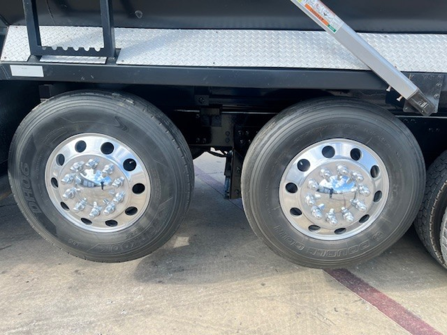 Two rear wheels of a Mack GU713 dump truck showing chrome hub covers and dual tires under a dump bed.