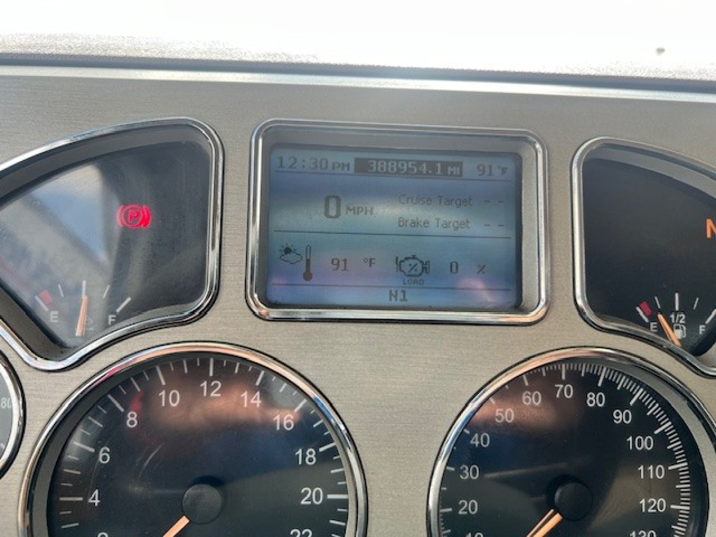 Dashboard of a Mack GU713 truck showing digital display with 0 MPH, 91°F, 12:30 PM, Brake Target, and various gauges; left and right gauges and warning lights visible.