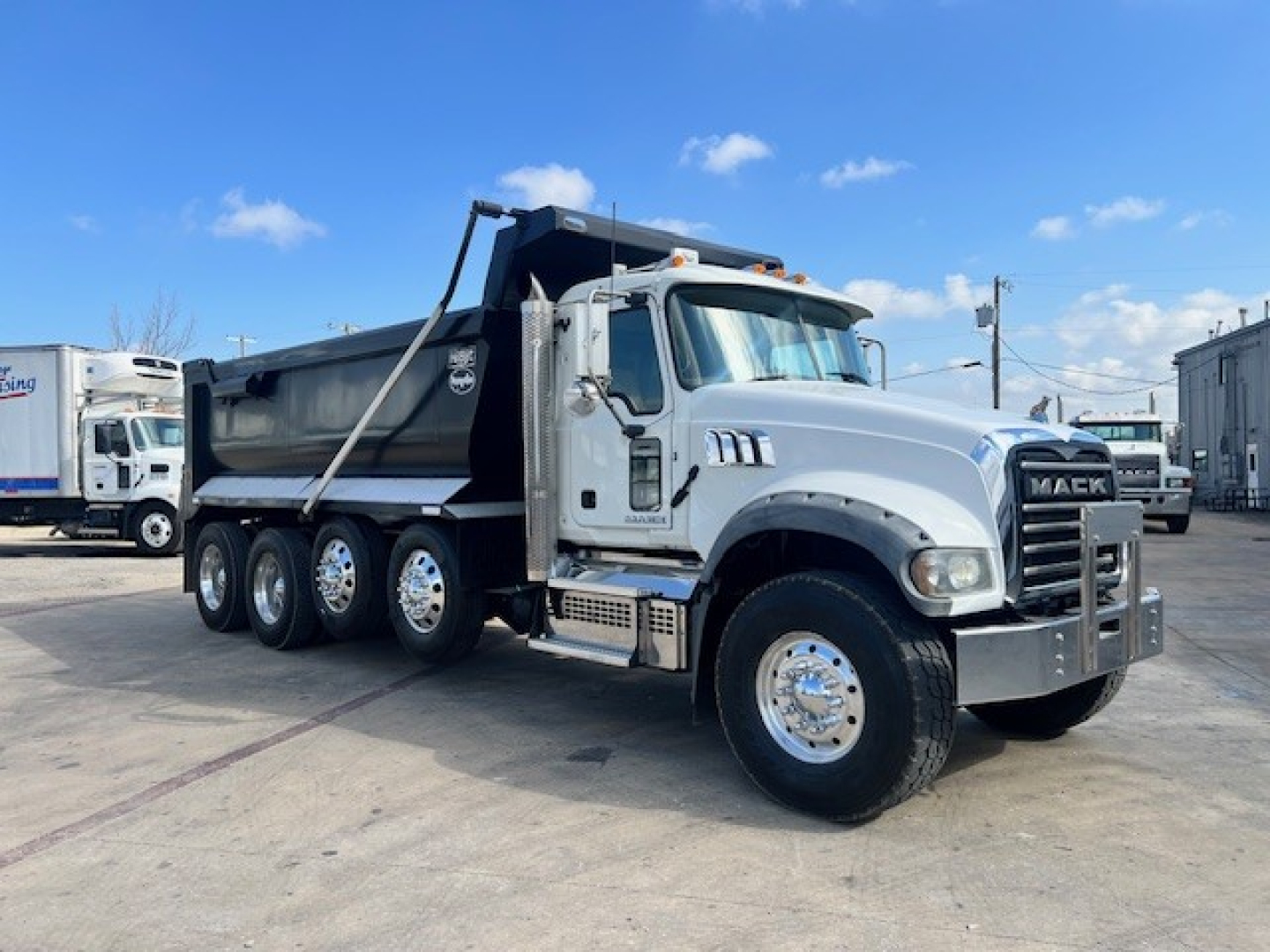 Dump truck with Mack GU713 front, silver/gray color, showing side view with multiple rear axles and the dump bed in raised position.