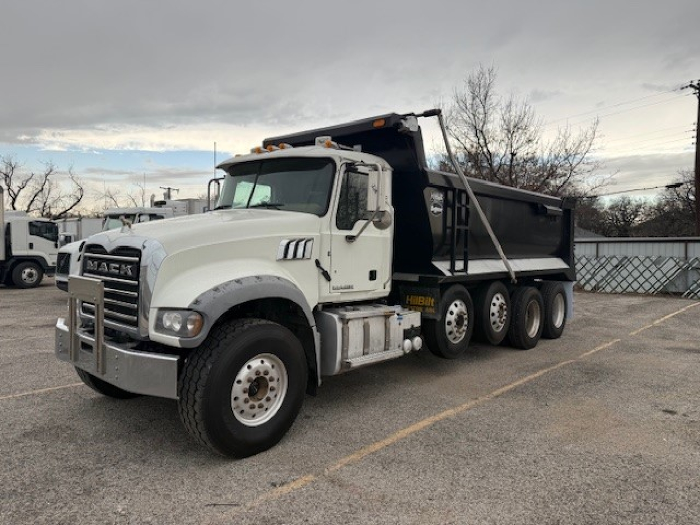 Mack GU713 dump truck in white cab with black dump body, front grille and bumper visible, VIN plate not legible, side drills and dual rear axles.
