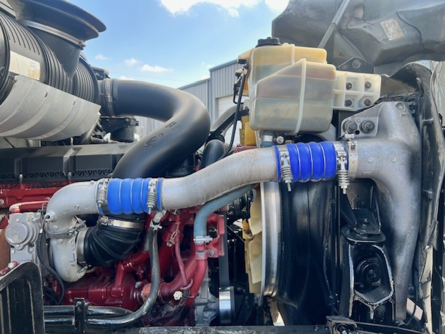 Mack GU713 engine bay showing coolant reservoir, radiator, intercooler piping, blue silicone couplers, and coolant expansion tank.