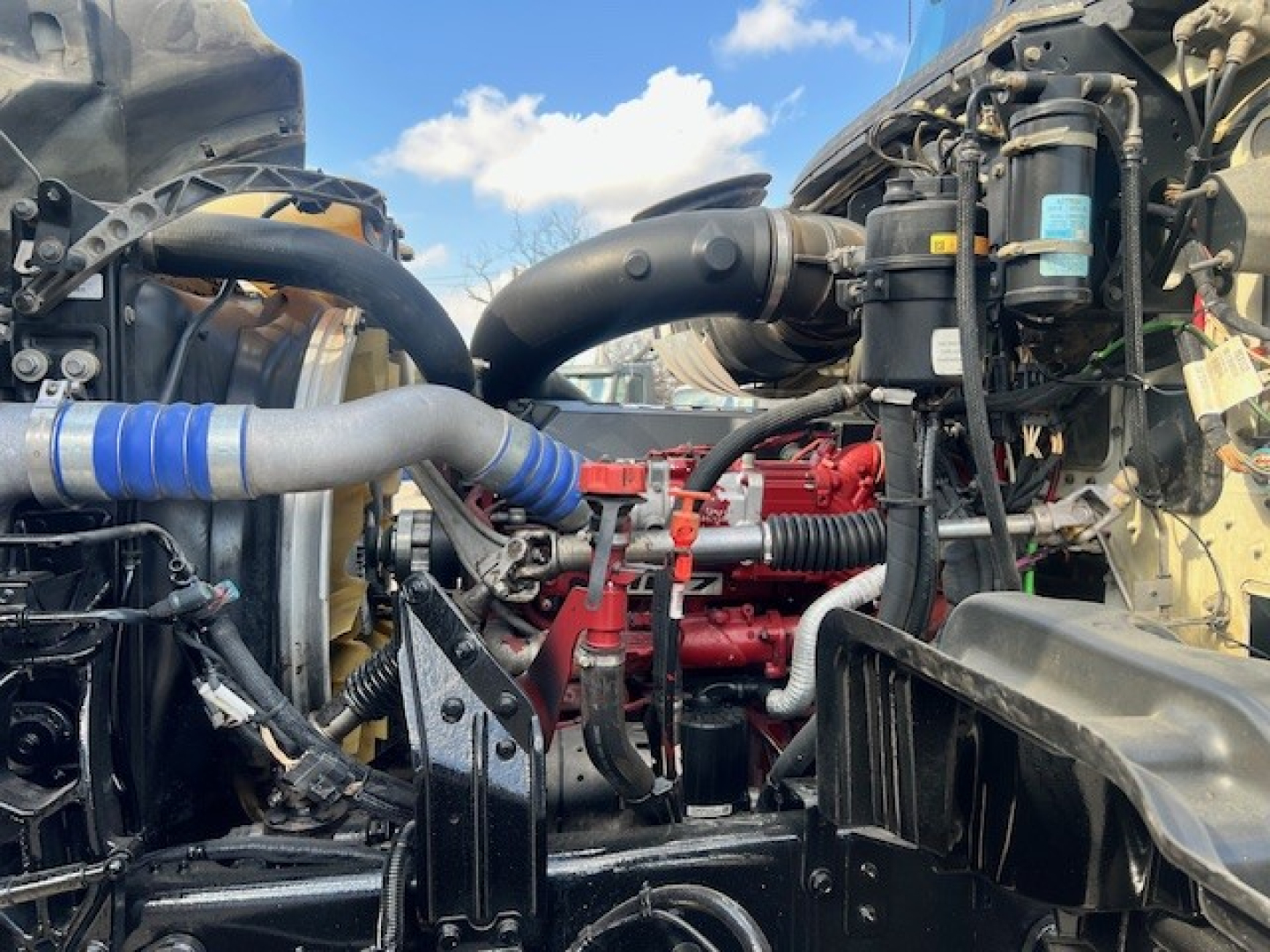 Mack GU713 engine bay view showing red engine block, black hoses, and cooling components; visible labels on filter canisters and wiring harnesses in compact layout.