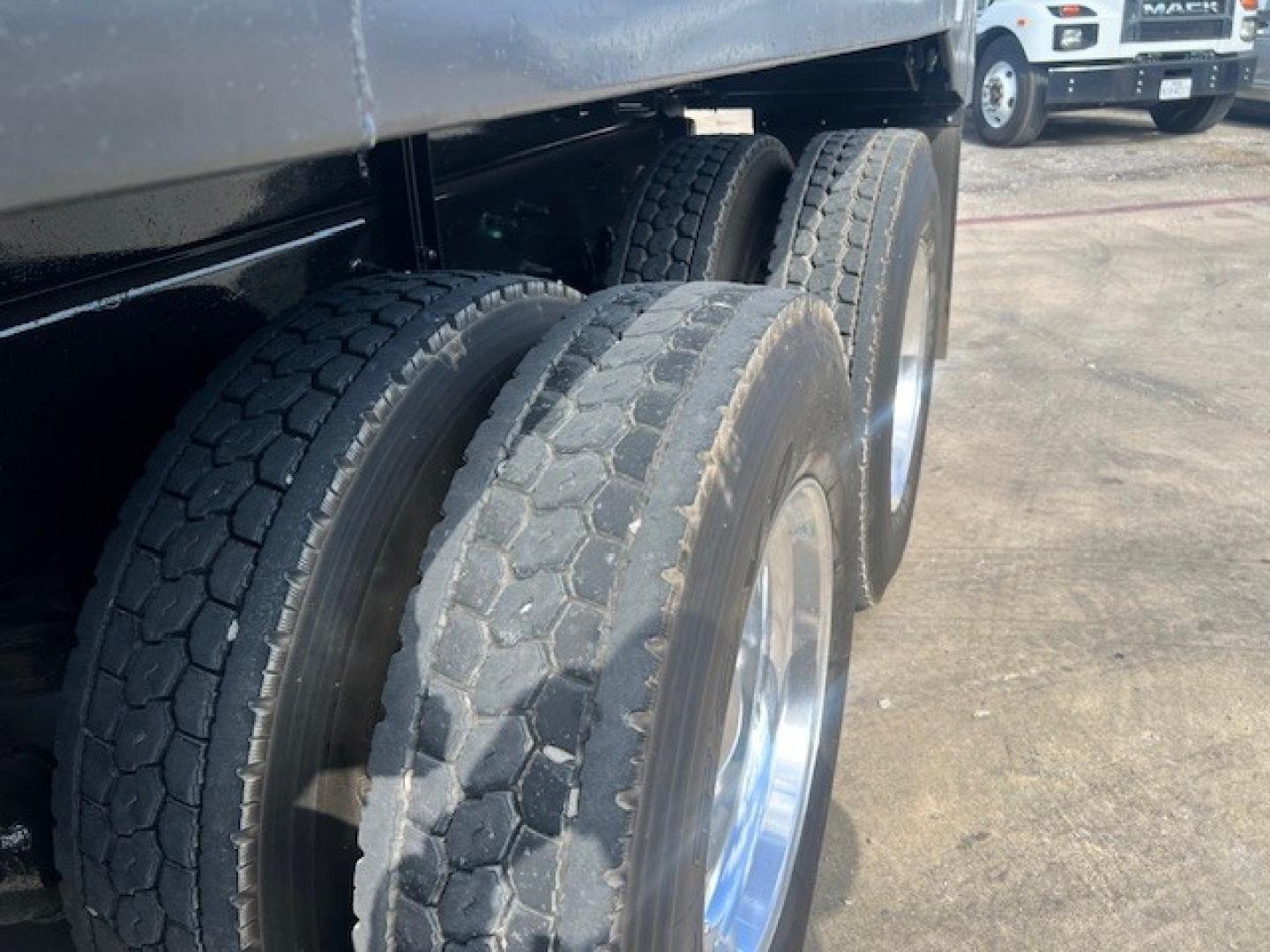 Rear dual-wheel area of a Mack GU713 dump truck showing triple axle tires and metal rims.