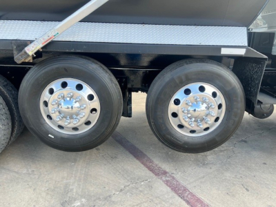 Dual rear axles with polished aluminum wheels on a dump truck; visible are tire treads and a metal step; no legible text other than reflections.