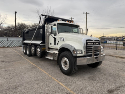 Dump truck front view showing Mack GU713 with white cab and black dump body, chrome bumper, dual rear axles, and heavy-duty tires.