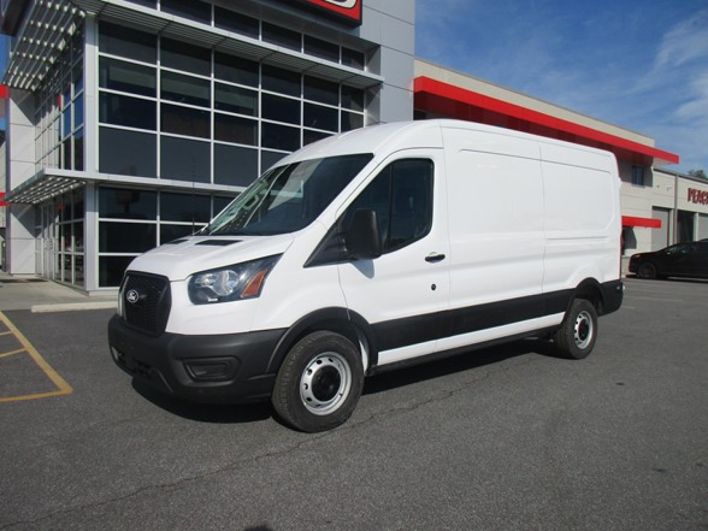 Ford Transit cargo van in a dealership lot, white exterior, black bumper, side view with short wheelbase.