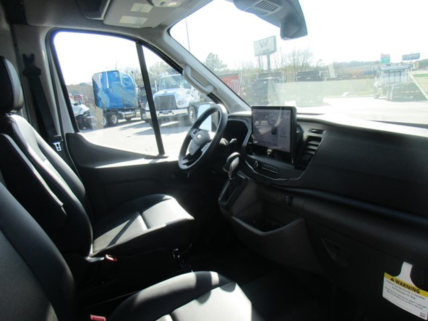 Ford Transit cargo van interior driver seat view showing steering wheel, dashboard, and touchscreen display.