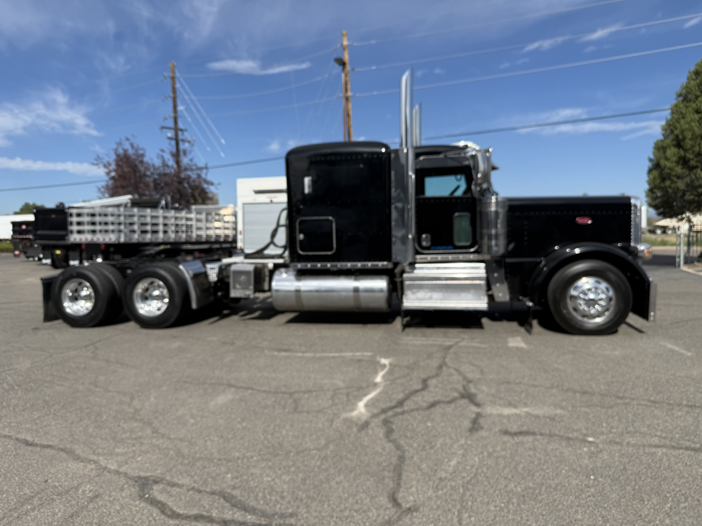 Peterbilt 389 conventional sleeper truck side view showing black cab, chrome fuel tanks, and dual rear axles with flatbed trailer.