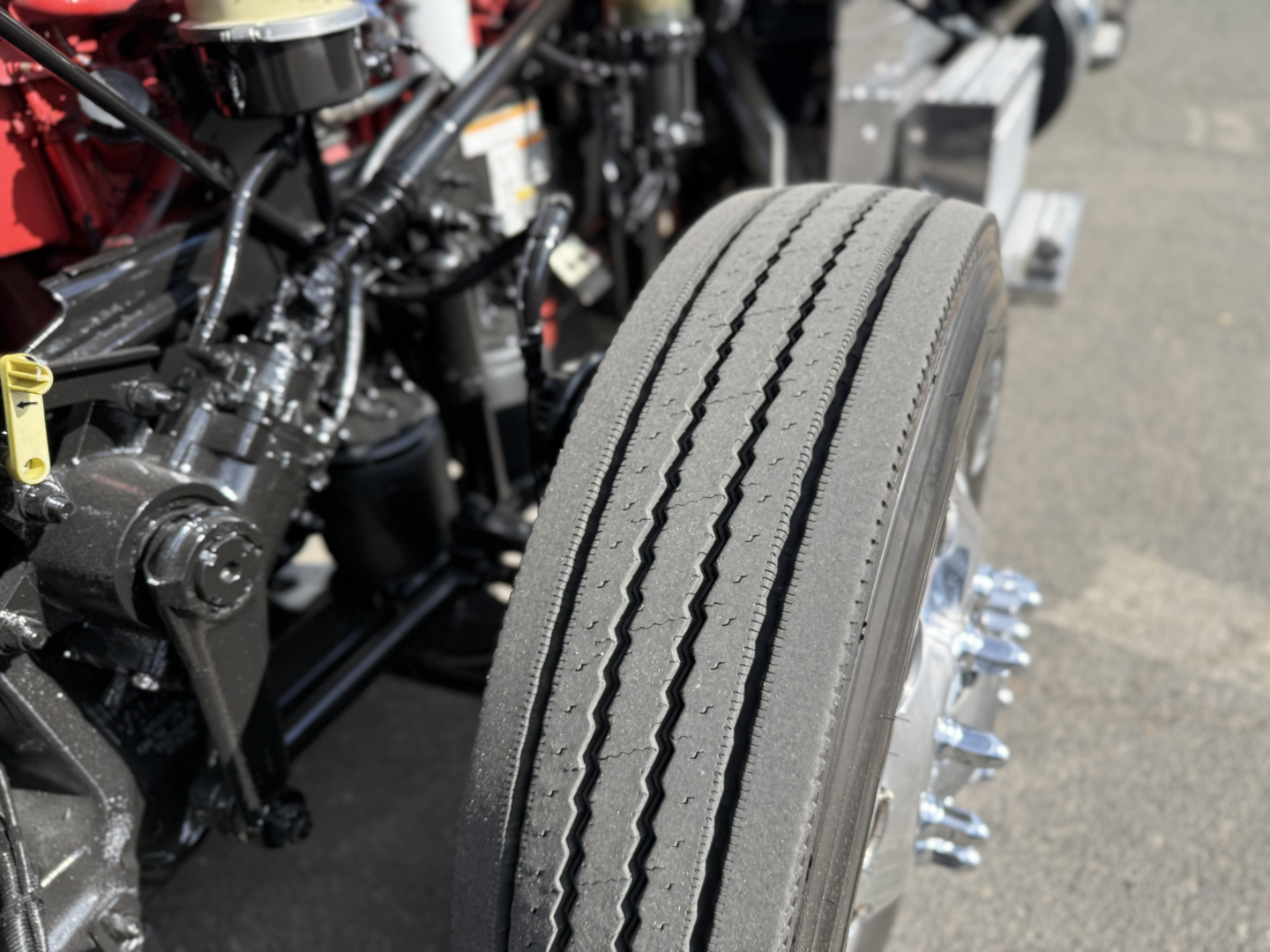 Peterbilt 389 engine bay and front wheel showing treaded tire, chrome lug nuts, and mechanical components.