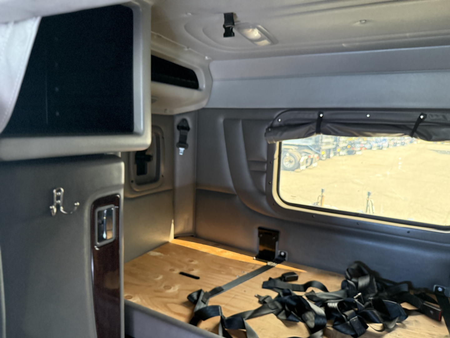 Peterbilt 389 sleeper cab interior with side window, storage cabinet, and seat belts laid on wooden floor panel