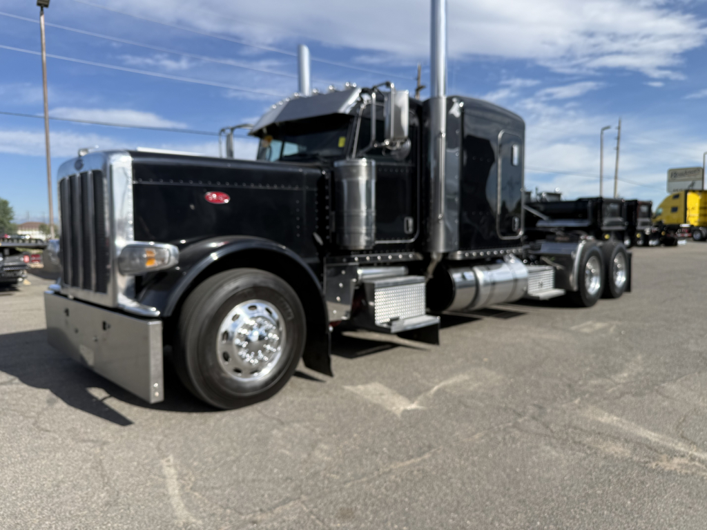 Peterbilt 389 conventional sleeper truck in black, side view showing chrome fuel tanks, steps, and dual rear axles.