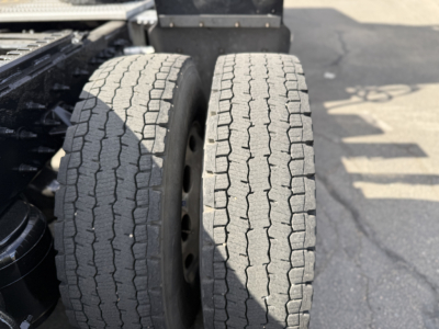 Two rear tractor tires visible with tread and wheel rims; portion of chassis and ground.