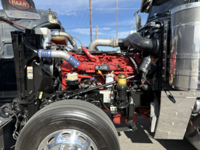 Peterbilt 389 engine bay with red Cummins/engine block, hoses, and front left wheel visible