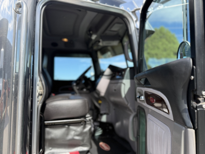 Peterbilt 389 truck cab interior view through open driver door showing steering wheel, dashboard, and seating area.