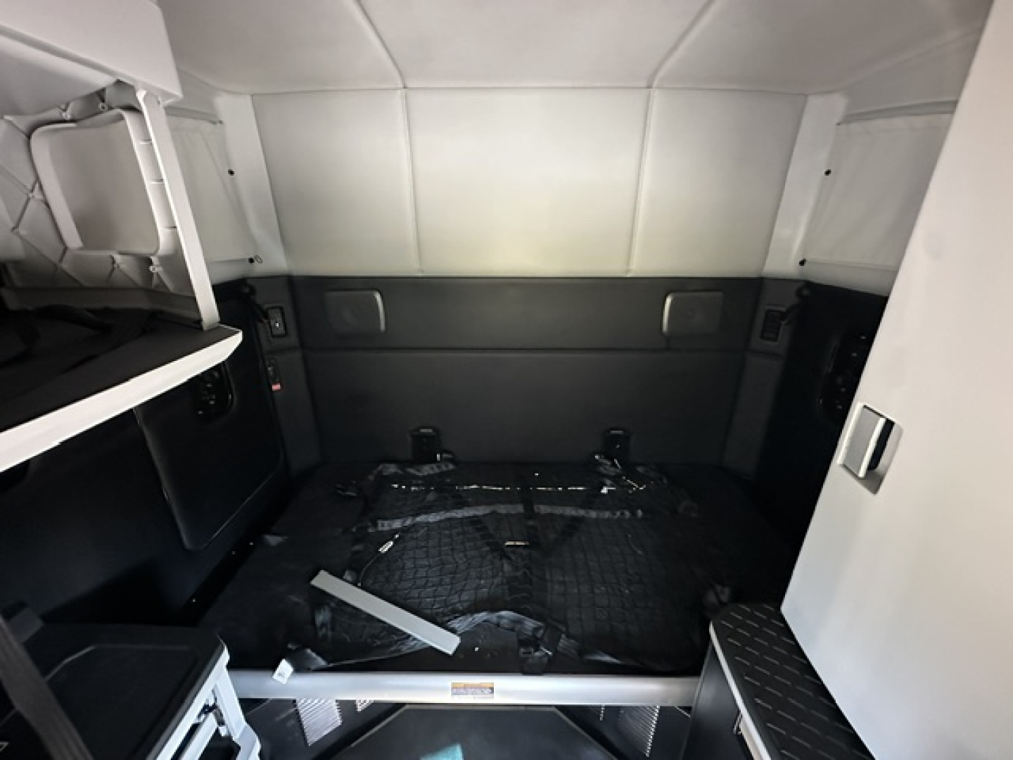 Kenworth T680 sleeper cab interior cargo area showing bare space with black protective mat and storage alcove.