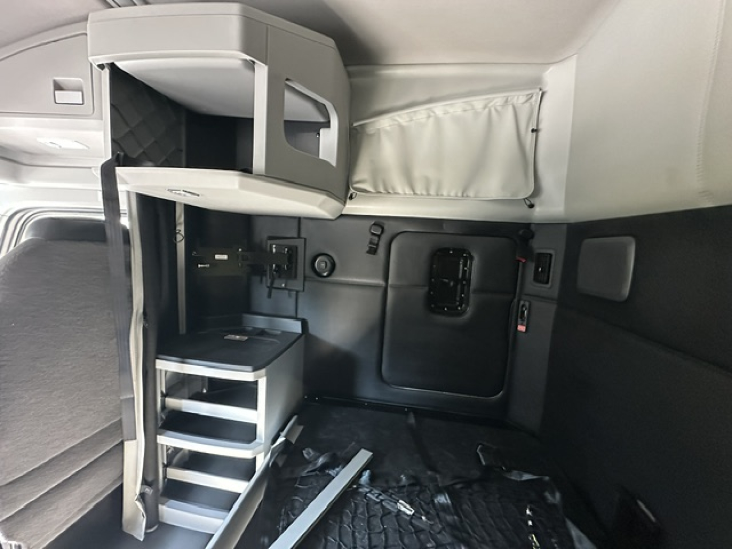 Kenworth T680 sleeper cab interior showing upper bunk storage shelf and side ladder with steps and a fold-down desk area.