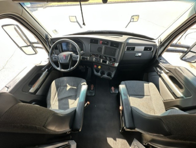 Interior of a 2023 Kenworth T680 cab from the driver perspective, showing steering wheel, dashboard with gauges and controls, two front seats, and center console.