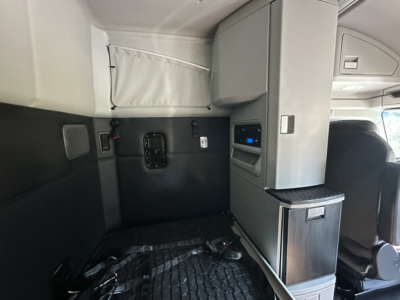 Kenworth T680 sleeper cab interior showing side cabinet with storage, control panel, and upper bunk area.