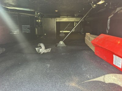 Kenworth T680 undercarriage view showing storage and tools including red toolbox and floor mat.