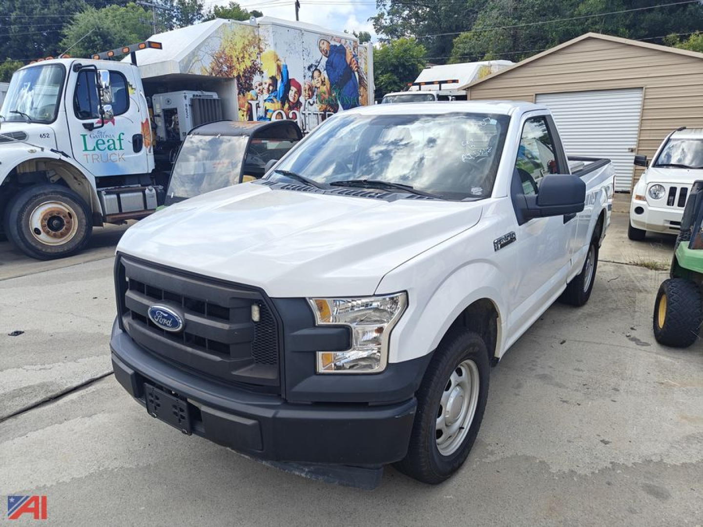 White Ford F-150 pickup truck shown from front-left view, with black front bumper and grille, Ford emblem on grille, side mirror, and truck bed visible; background includes other vehicles and a mural.
