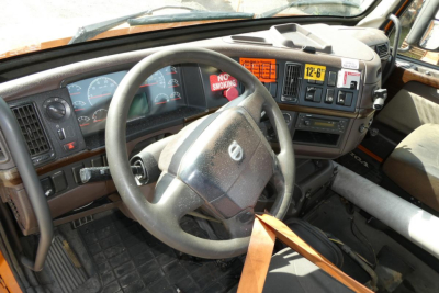 Volvo truck cab interior showing steering wheel and dashboard with gauges and control panel, gear area, and sun visor in view.