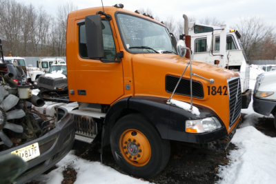 Volvo VNM42T conventional daycab truck in orange with black fenders, number 1842 on door, snow-covered ground.