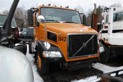 Volvo VNM42T conventional daycab truck in orange showing VIN plate and front grille with Volvo logo.
