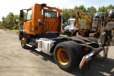 Volvo VNM42T truck tractor in service showing side view with orange cab and chassis, fuel tanks, and rear wheel wells.