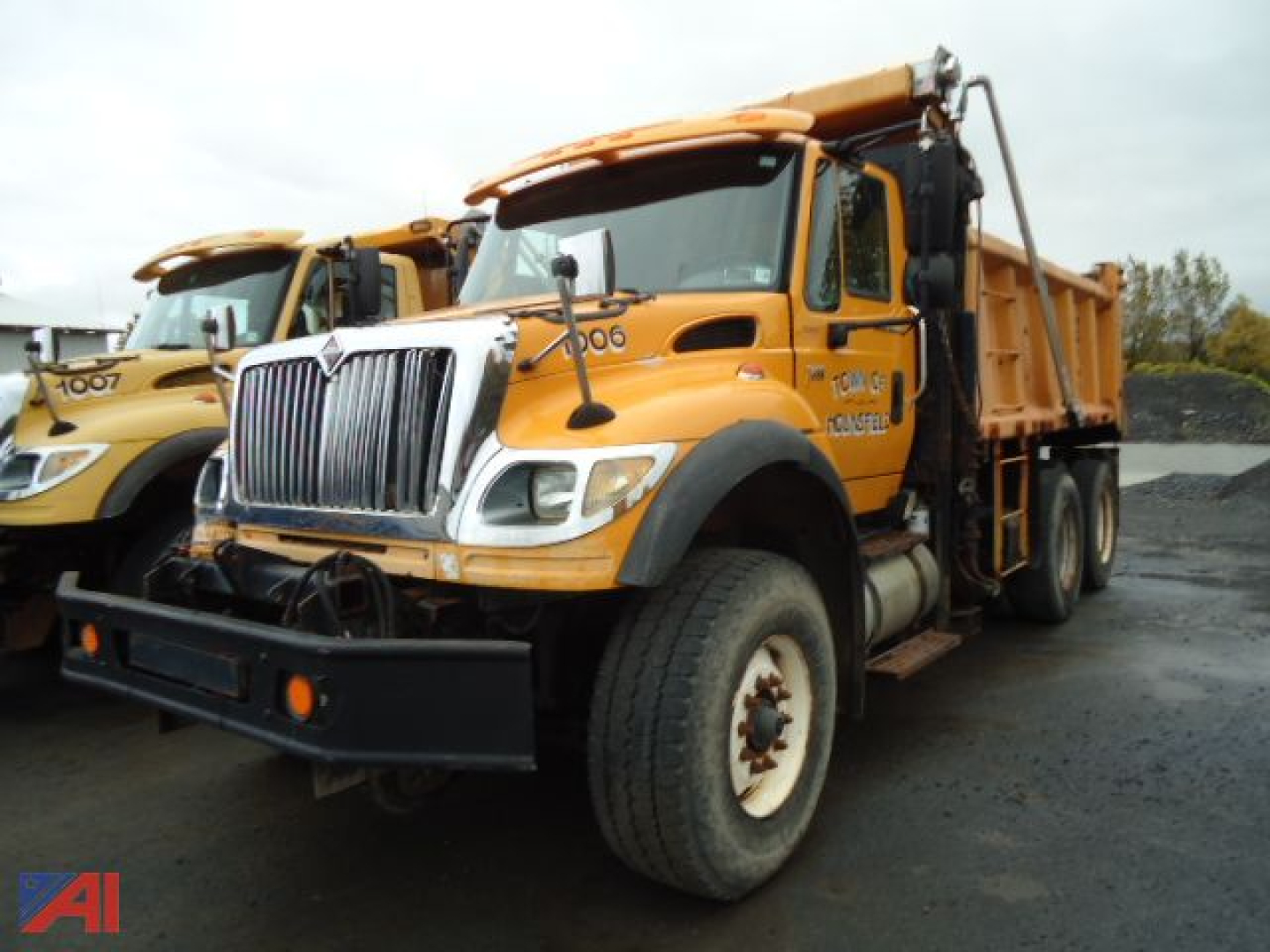 International WorkStar 7600 dump truck with orange cab and chassis, front grille, large dual rear wheels, and dump bed visible.
