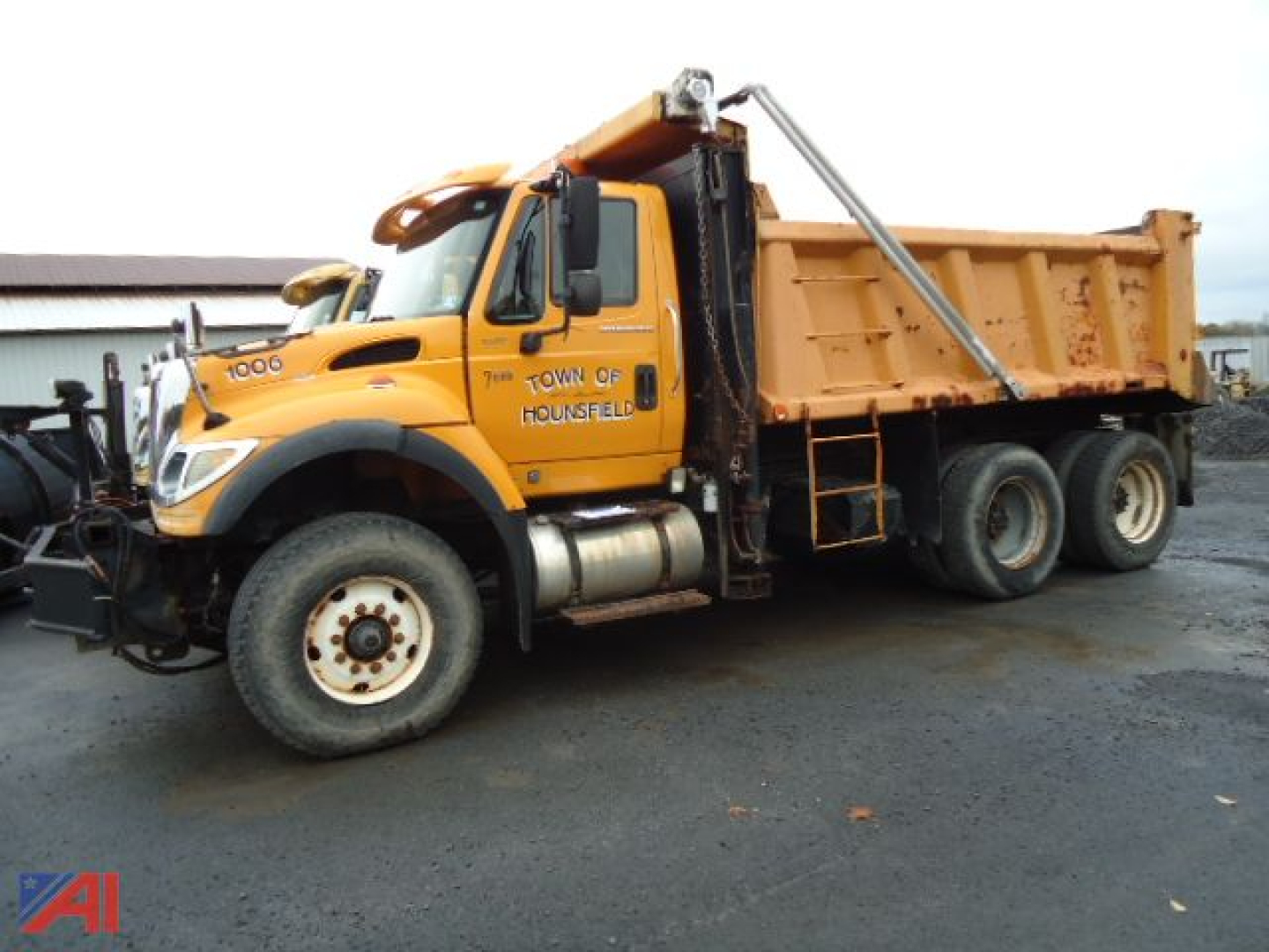 Dump truck with orange cab and dump bed showing side text 'TOWN OF HOUNSFIELD' and International logo.