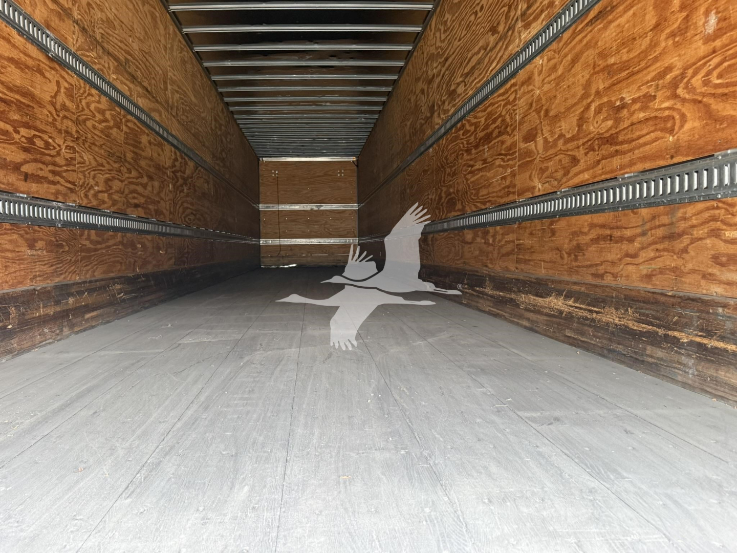 Inside cargo trailer showing empty wooden side walls and metal rails, bare floor, perspective toward the far end.
