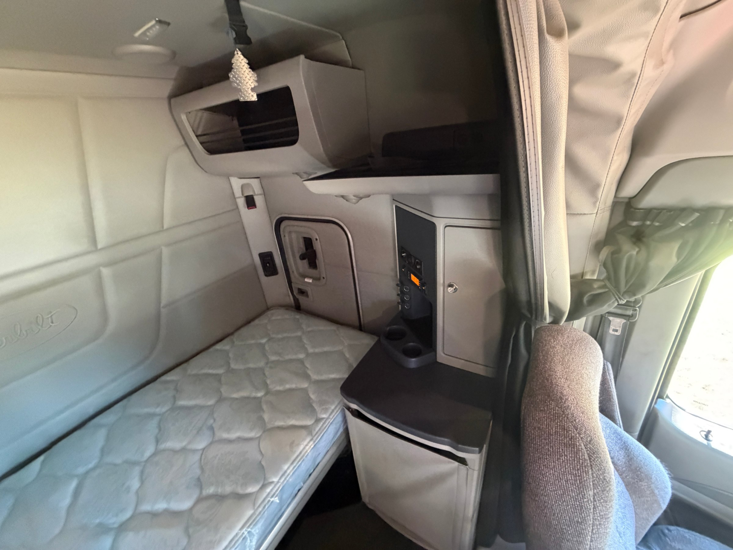 Truck sleeper cab interior with quilted mattress, overhead bunk area, and control panels in a Peterbilt 579 cab.