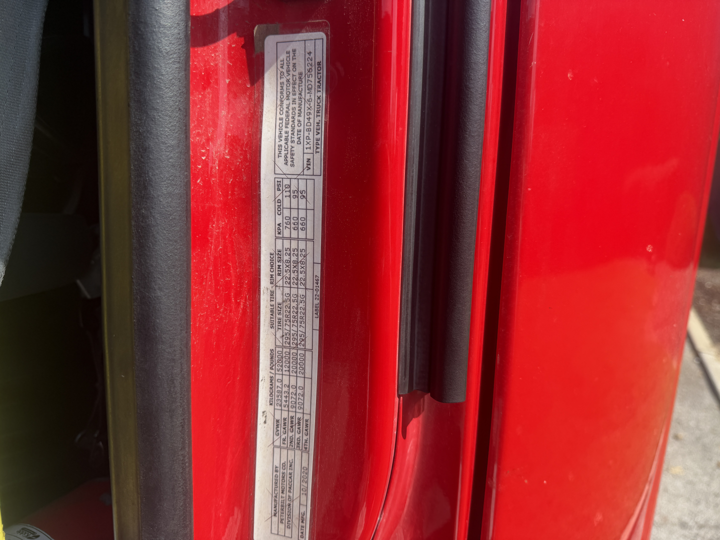 Vehicle door jamb label with compliance and spec text on a red Peterbilt truck. Includes small printed table data