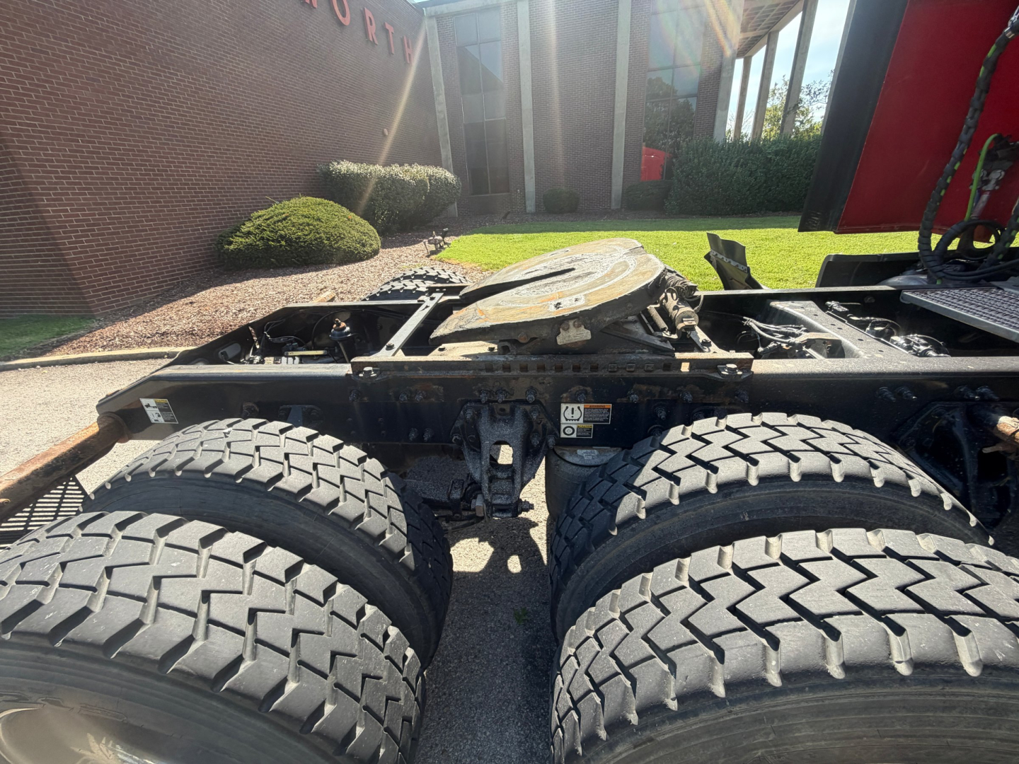 Peterbilt 579 chassis with dual rear axles and heavy-duty tires, fuel/tank area and drive train visible, view from side of truck cab with platform and mud flaps.