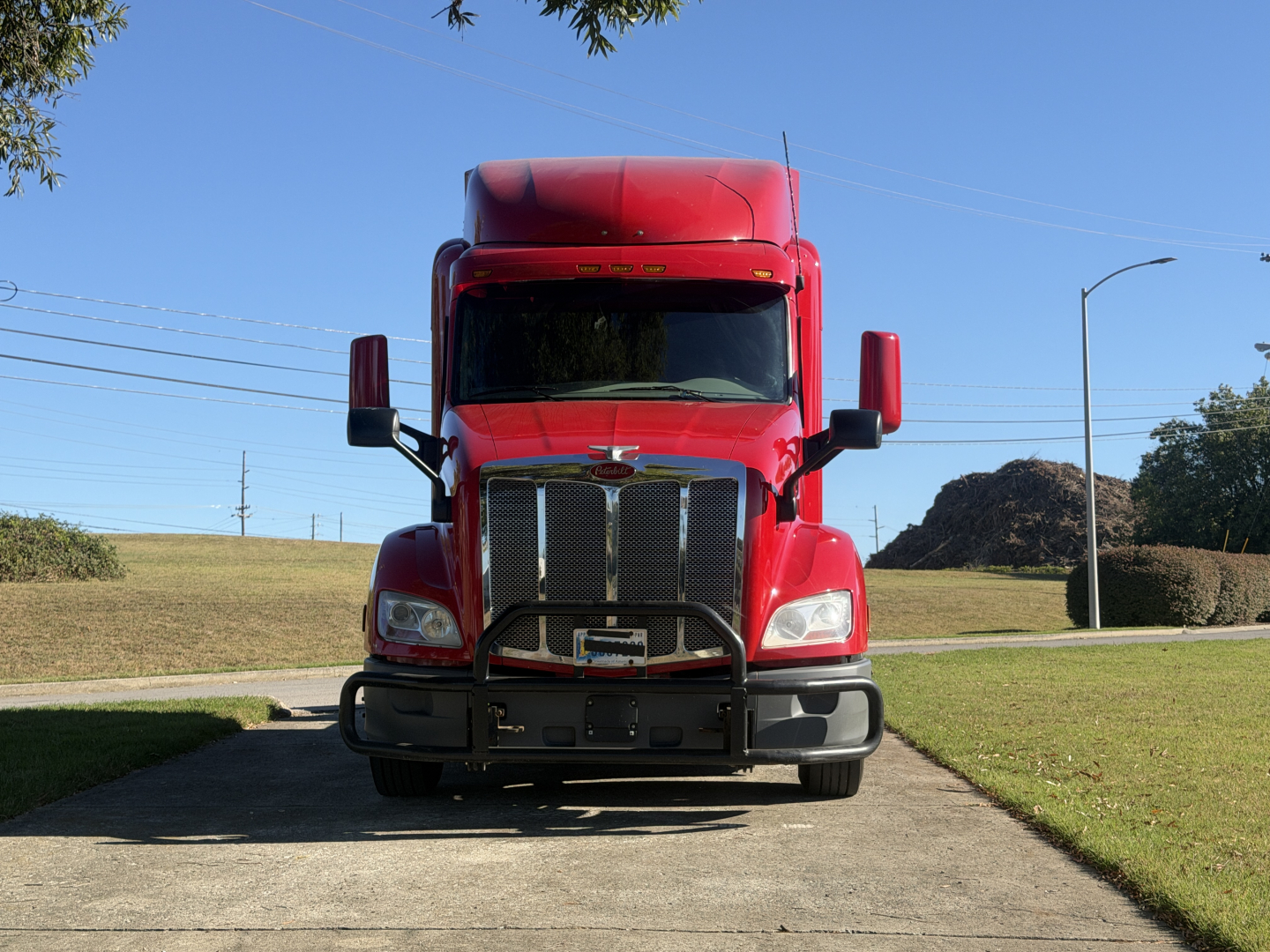 Peterbilt 579 truck front view in red with large grille and bumper, headlamps, side mirrors, and highway in background.