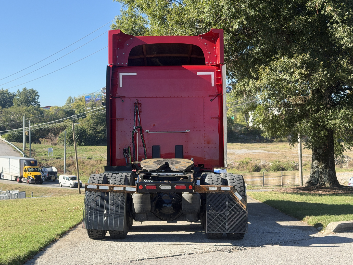 Rear view of a red Peterbilt 579 tractor with empty dump bed, showing dual rear axles and mud flaps.