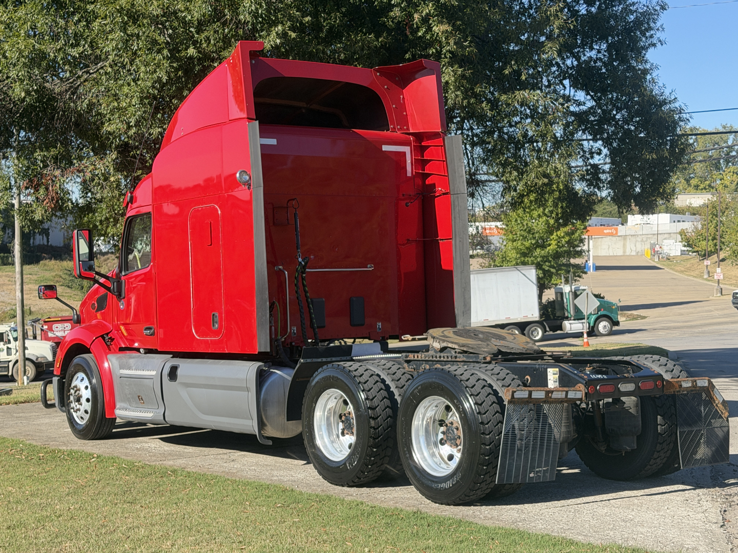 Peterbilt 579 tractor unit in red with sleeper cab, viewed from side rear showing sixth-wheel tandem and open rear deck.