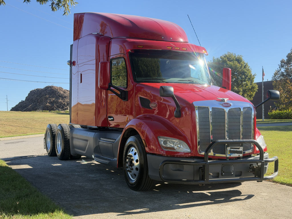 Peterbilt 579 conventional sleeper truck in red, front-right view showing chrome grille, bumper guard, and dual rear axles.