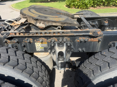 Peterbilt 579 truck chassis showing fifth wheel and dual rear wheels, with visible hoses, frame rails, and warning labels on the center section.