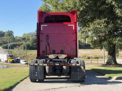 Rear view of a red Peterbilt 579 tractor with empty dump bed, showing dual rear axles and mud flaps.