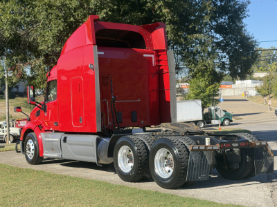 Peterbilt 579 tractor unit in red with sleeper cab, viewed from side rear showing sixth-wheel tandem and open rear deck.