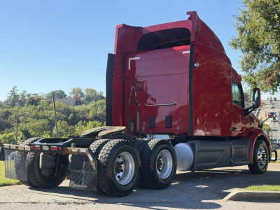 Peterbilt 579 tractor cab rear view showing chassis and dual rear axles with fifth wheel, red exterior, side fuel tanks, and skyline sleeper.