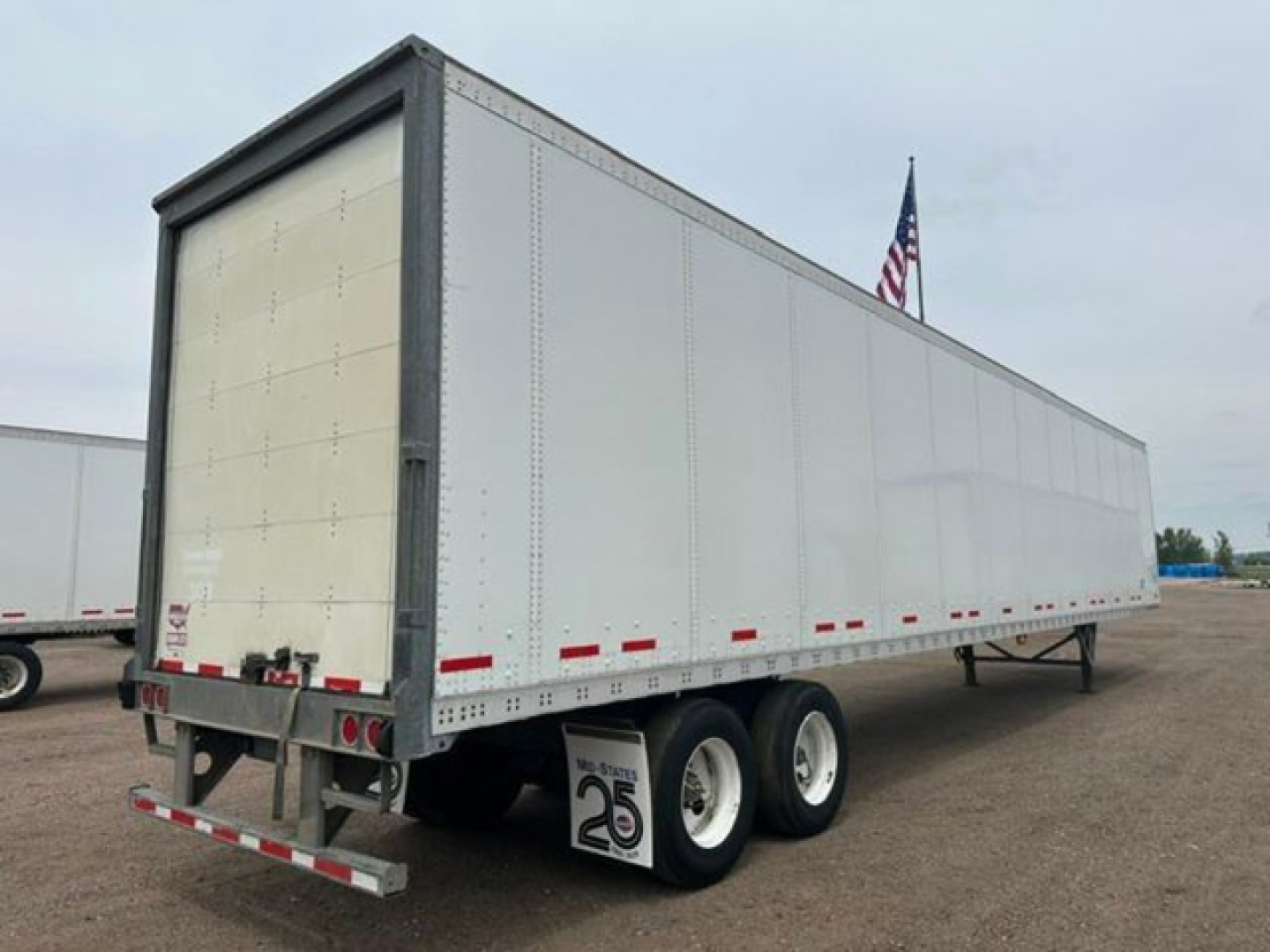 Trailer side and rear view showing a 2016 Wabash van trailer with dual rear wheels, white exterior, and reflective tape along the lower edge.